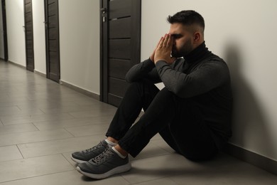 Photo of Sad man sitting on floor in hall. Space for text