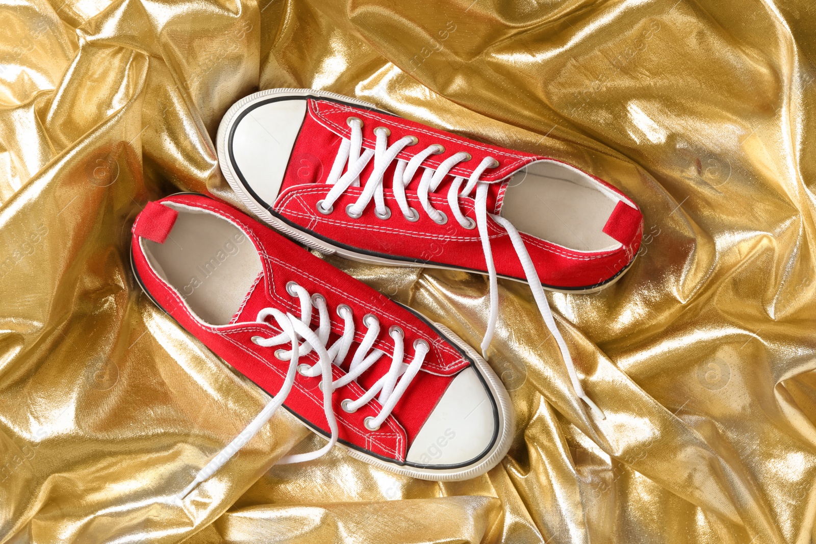 Photo of Pair of stylish shoes with laces on gold fabric, flat lay