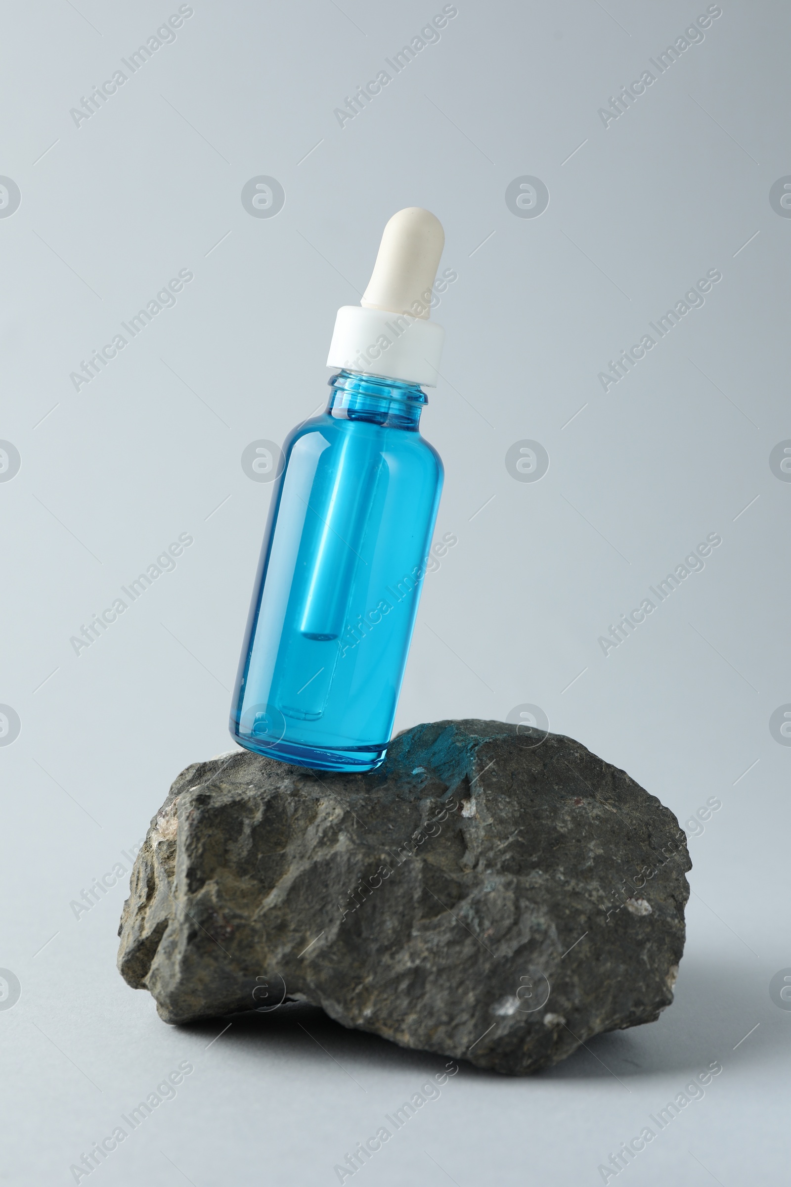 Photo of Bottle of cosmetic serum on stone against light grey background