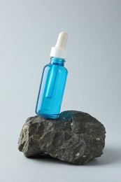 Bottle of cosmetic serum on stone against light grey background