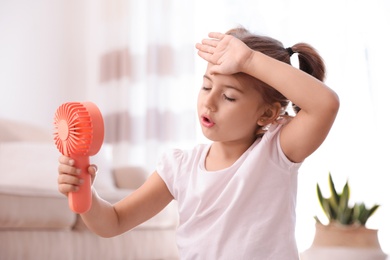 Photo of Little girl enjoying air flow from portable fan in living room. Summer heat