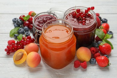 Jars with different jams and fresh fruits on white wooden table