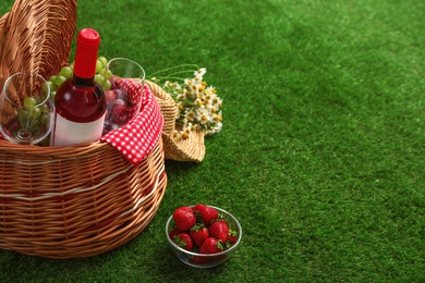 Picnic basket with wine and fruits on grass. Space for text