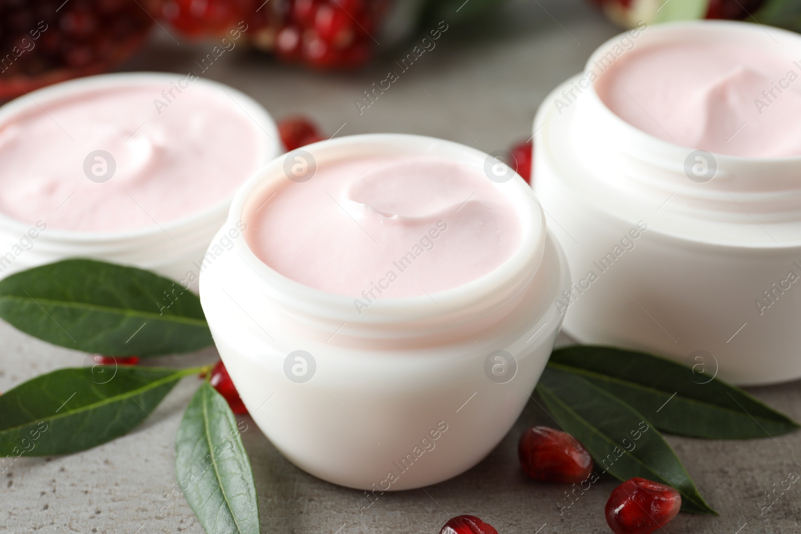 Photo of Natural facial mask, pomegranate seeds and green leaves on light grey table, closeup