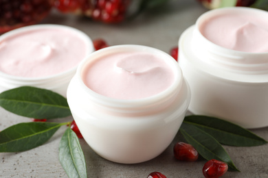 Natural facial mask, pomegranate seeds and green leaves on light grey table, closeup