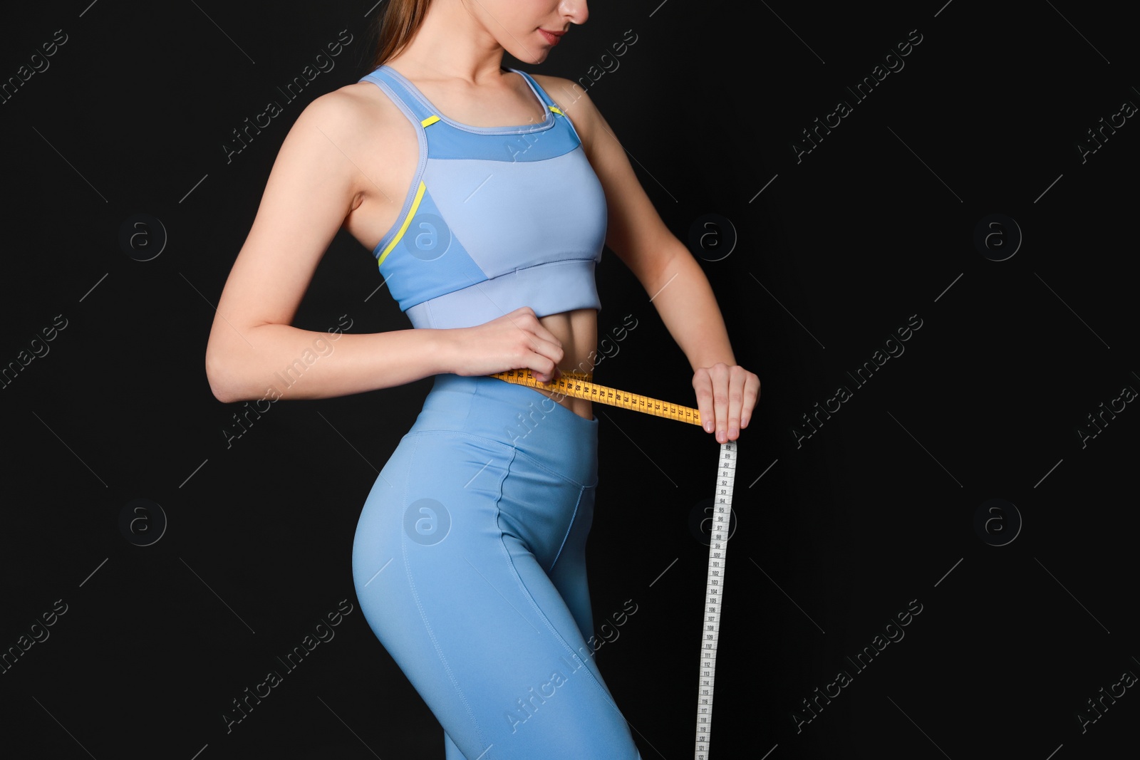 Photo of Woman in sportswear measuring waist with tape on black background, closeup. Space for text