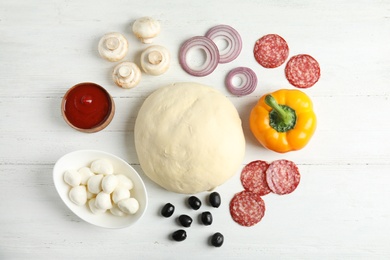 Flat lay composition with dough and ingredients for pizza on wooden table