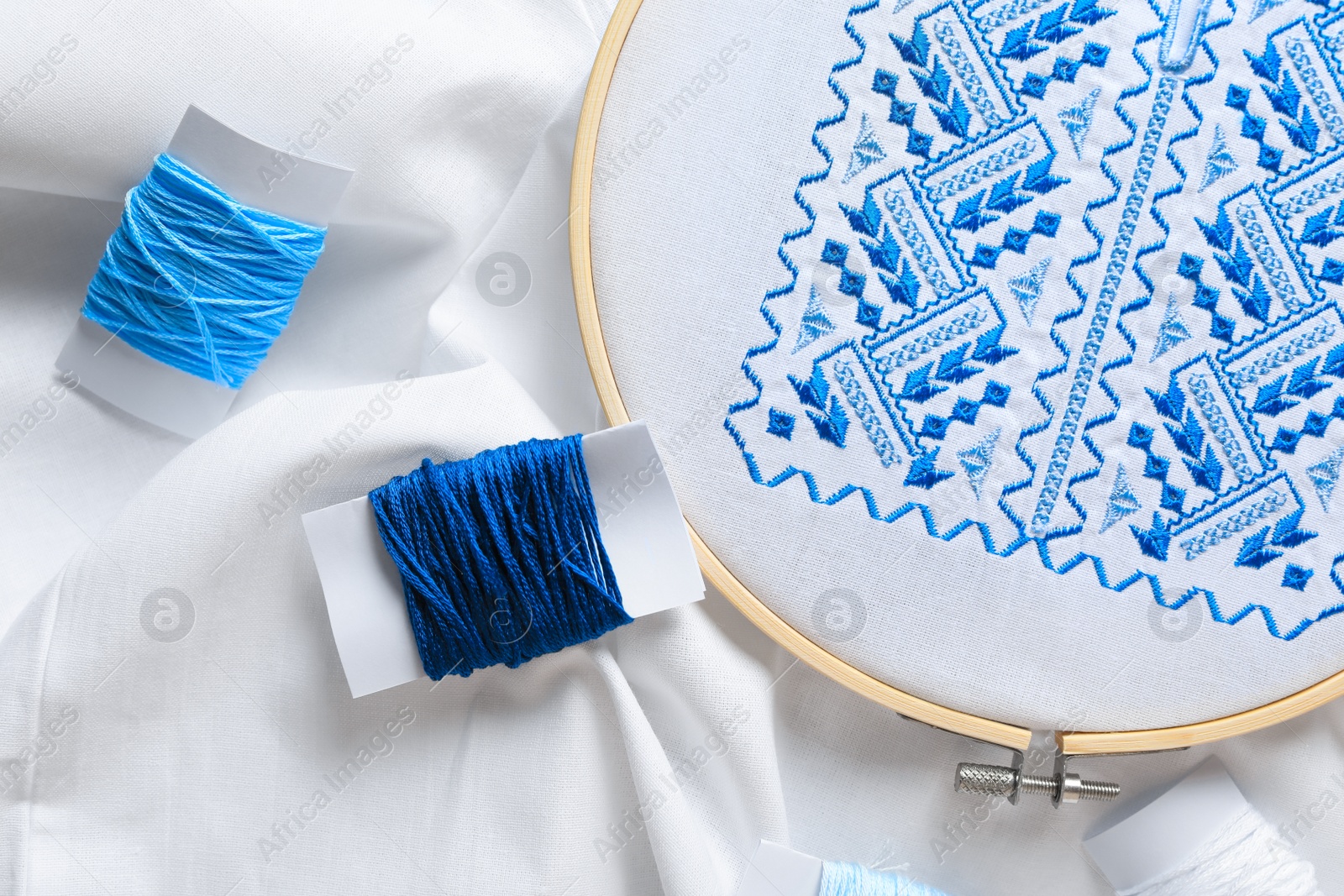 Photo of Threads and blue Ukrainian national embroidery on white fabric, top view