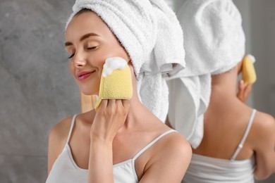 Happy young woman washing her face with sponge in bathroom