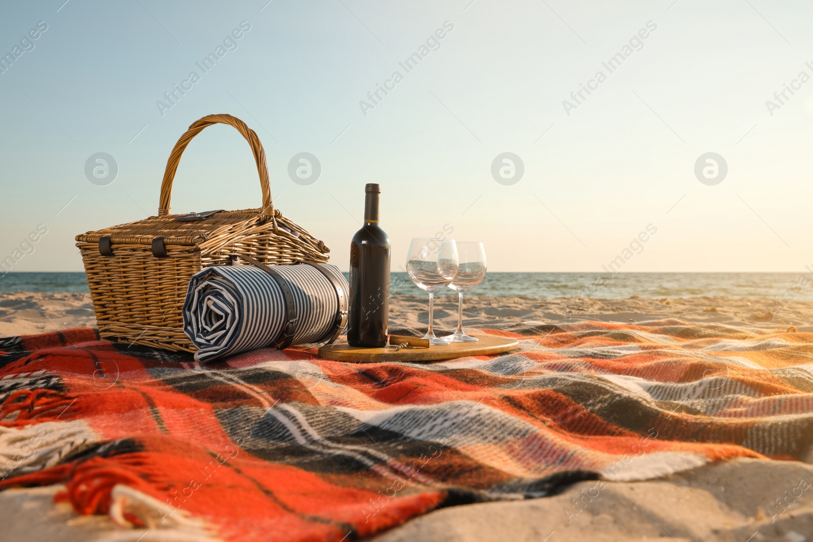 Photo of Blanket with picnic basket, bottle of wine and glasses on sandy beach near sea, space for text