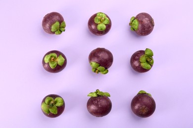 Photo of Fresh ripe mangosteen fruits on light violet background, flat lay