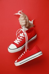 Photo of Woman holding pair of classic old school sneakers through hole in red paper, closeup