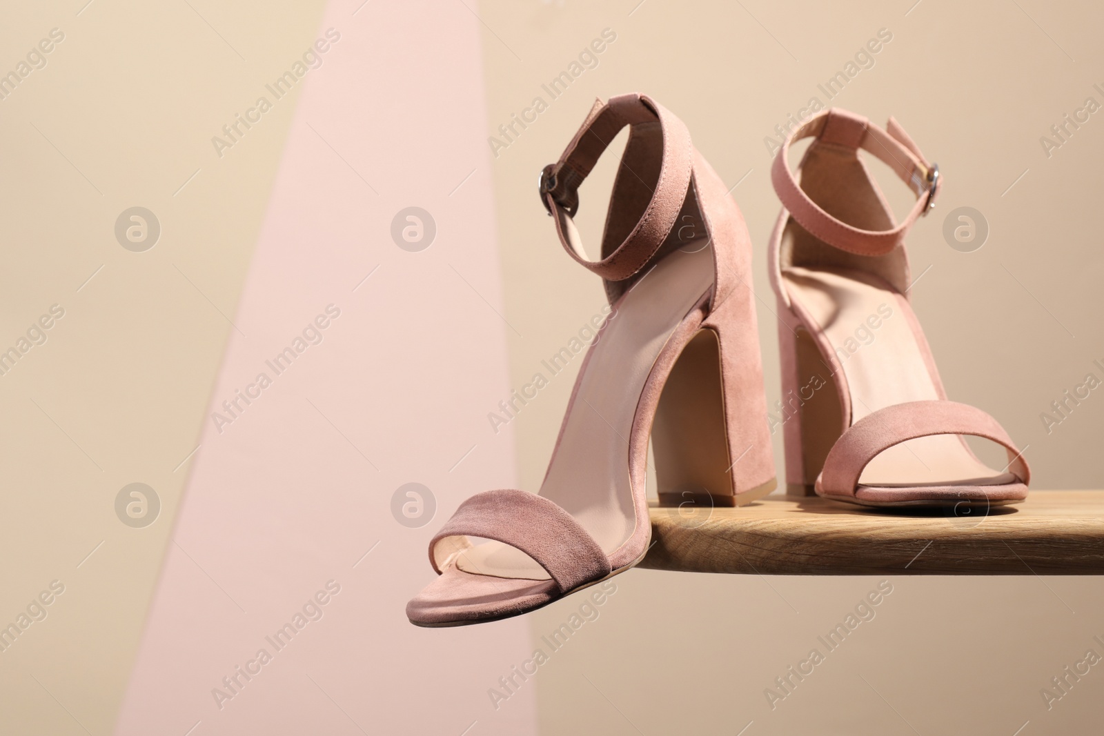 Photo of Pair of stylish high heeled shoes on wooden shelf against beige background, space for text