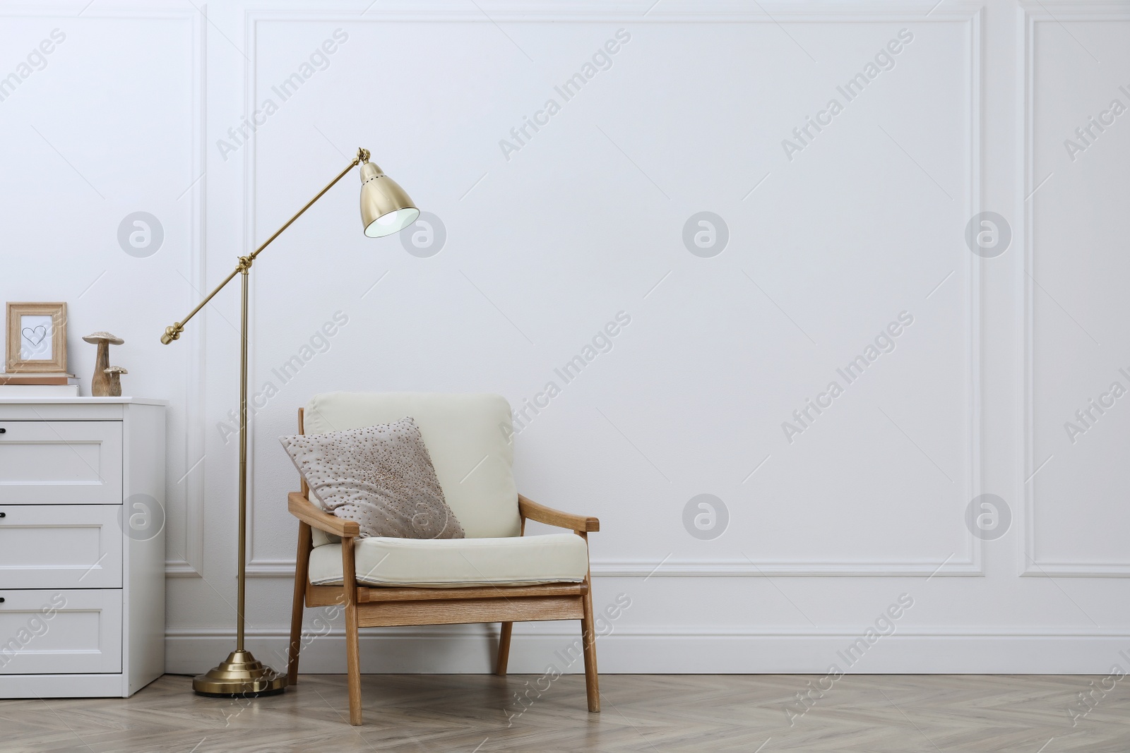 Photo of Stylish room interior with lamp, chest of drawers and armchair near white wall. Space for text