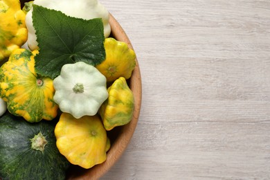 Photo of Fresh ripe pattypan squashes in bowl on light wooden table, top view. Space for text