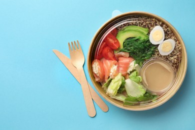 Photo of Tasty food in container with wooden fork and knife on light blue background, flat lay. Space for text