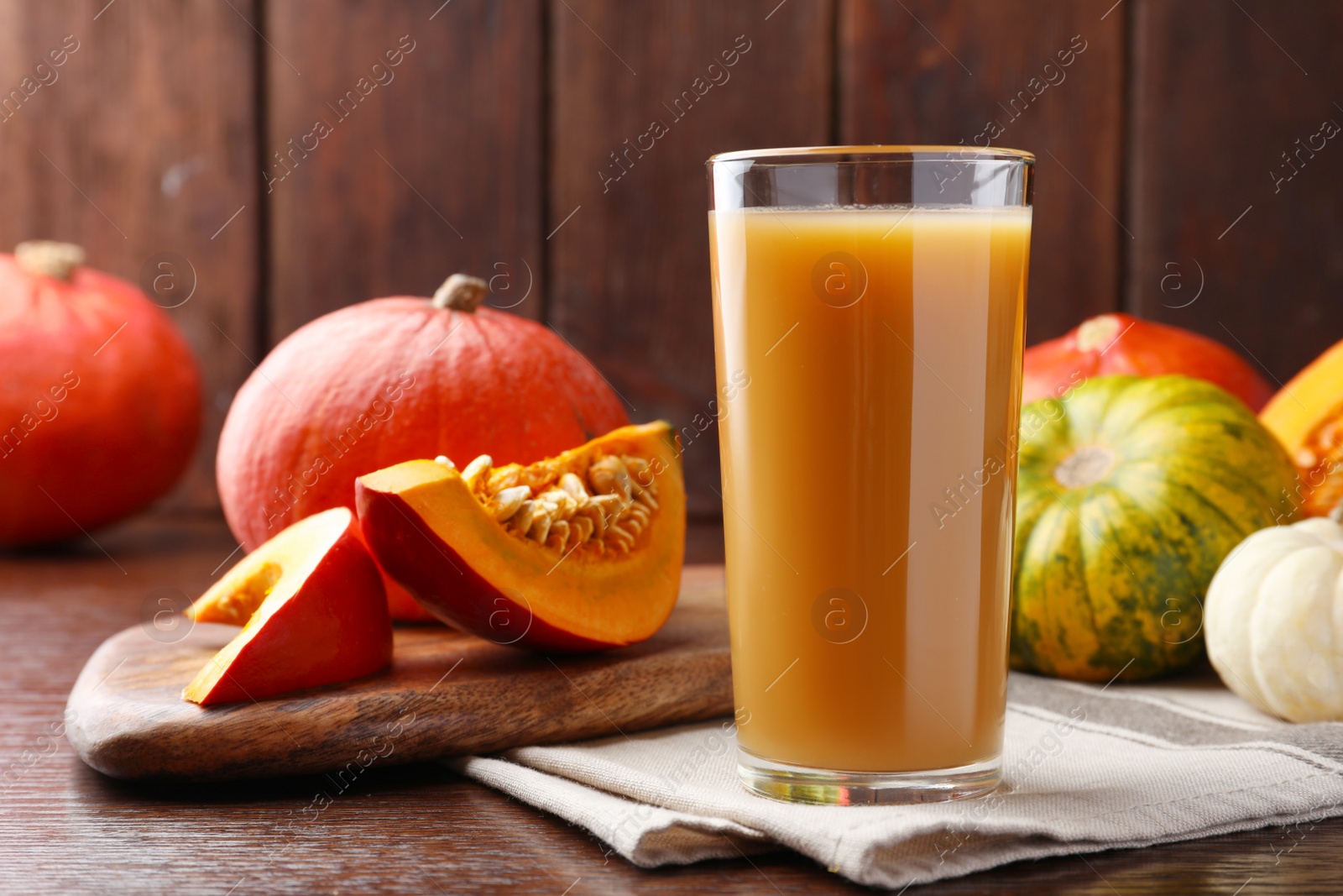 Photo of Tasty pumpkin juice in glass and different pumpkins on wooden table