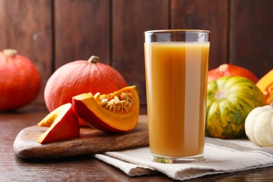 Photo of Tasty pumpkin juice in glass and different pumpkins on wooden table