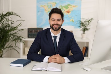 Happy manager with notebook sitting at desk in travel agency