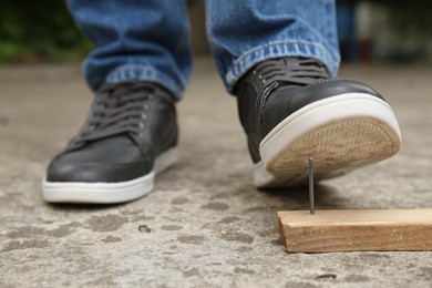 Photo of Careless man stepping on nail in wooden plank outdoors, closeup