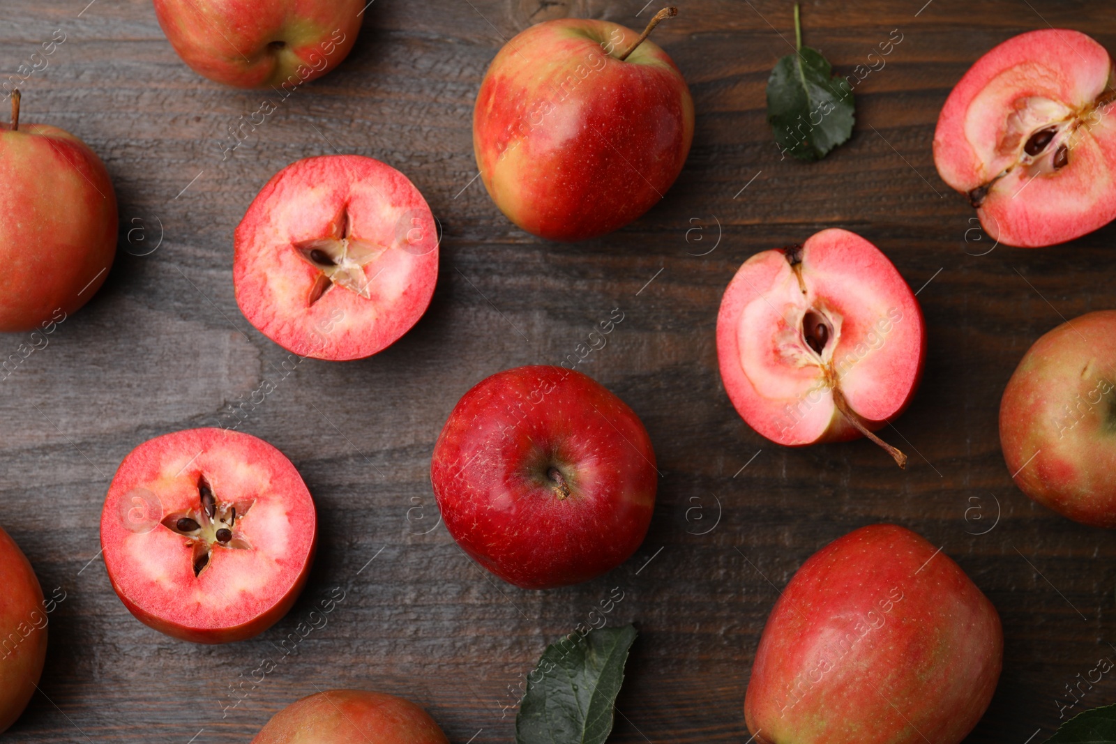 Photo of Tasty apples with red pulp and leaves on wooden table, flat lay