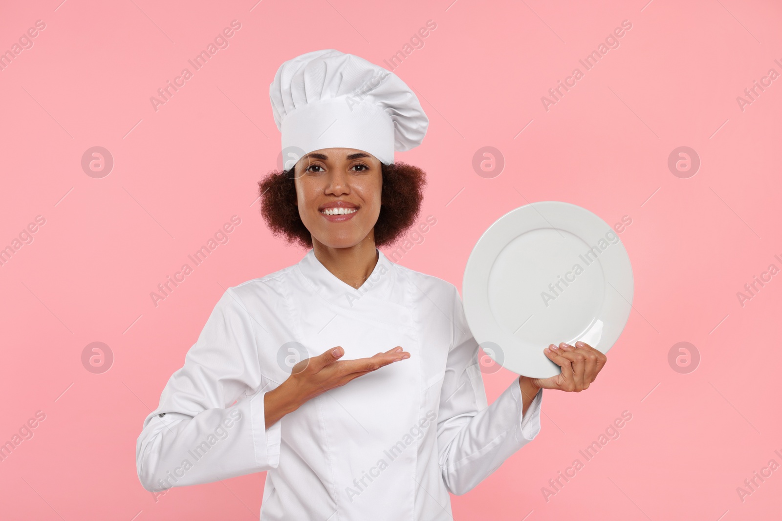 Photo of Happy female chef in uniform holding plate on pink background