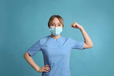 Photo of Doctor with protective mask showing muscles on light blue background. Strong immunity concept