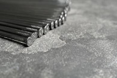 Photo of Pile of metal nails on grey stone background, closeup. Space for text