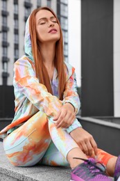 Photo of Beautiful woman in gym clothes sitting on parapet on street
