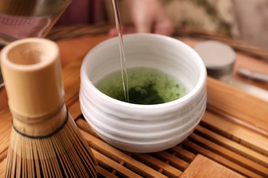 Photo of Chasen and pouring water into cup with matcha on wooden stand. Tea ceremony