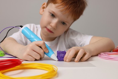 Boy drawing with stylish 3D pen at white table, selective focus