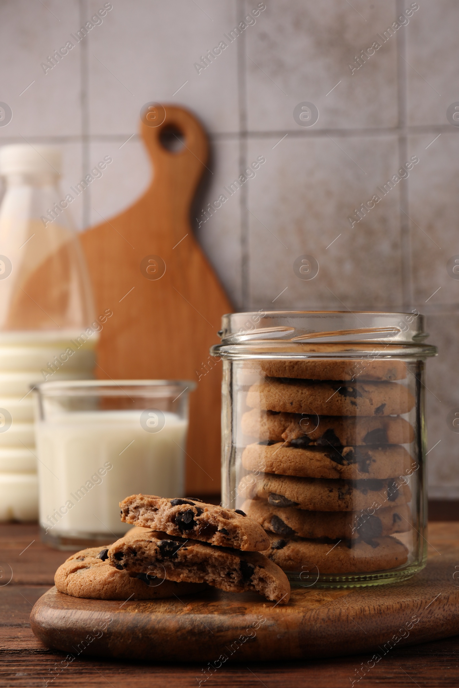 Photo of Glass jar with delicious chocolate chip cookies and milk on wooden table