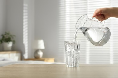 Photo of Woman pouring water from jug into glass at wooden table indoors, closeup. Space for text