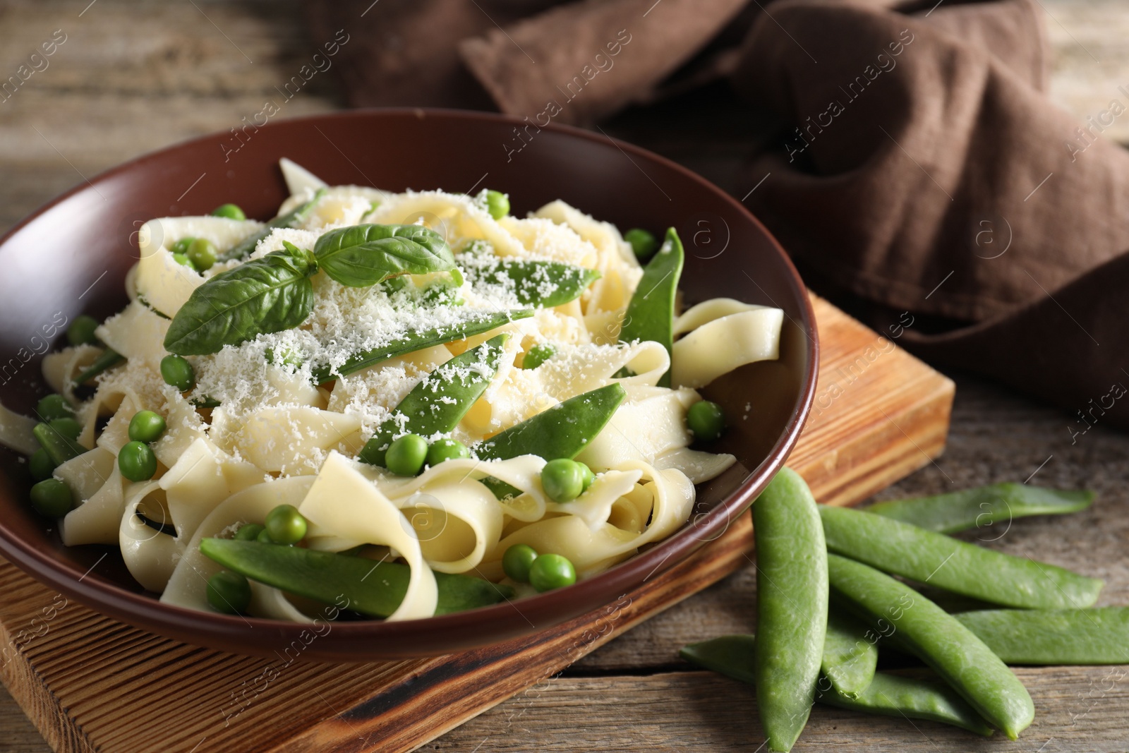 Photo of Delicious pasta with green peas, fresh basil and cheese on wooden table, closeup