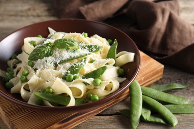 Photo of Delicious pasta with green peas, fresh basil and cheese on wooden table, closeup