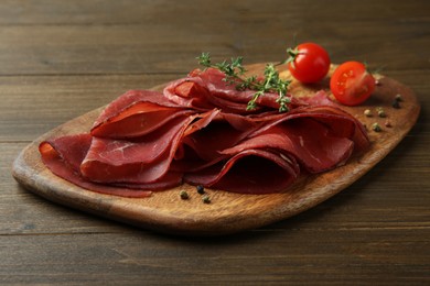 Photo of Tasty bresaola, peppercorns, tomatoes and thyme on wooden table