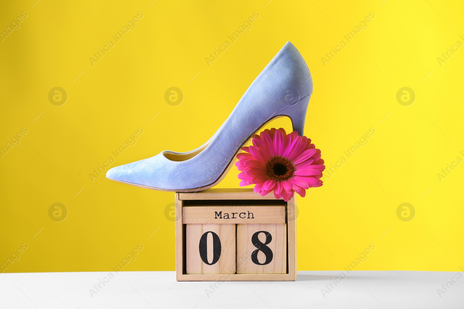 Photo of Stylish lady's shoe, flower and wooden block calendar on table against color background. International Women's Day