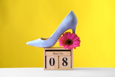 Photo of Stylish lady's shoe, flower and wooden block calendar on table against color background. International Women's Day