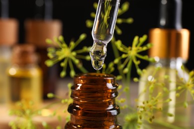 Photo of Dripping dill essential oil from pipette into bottle on blurred background, closeup