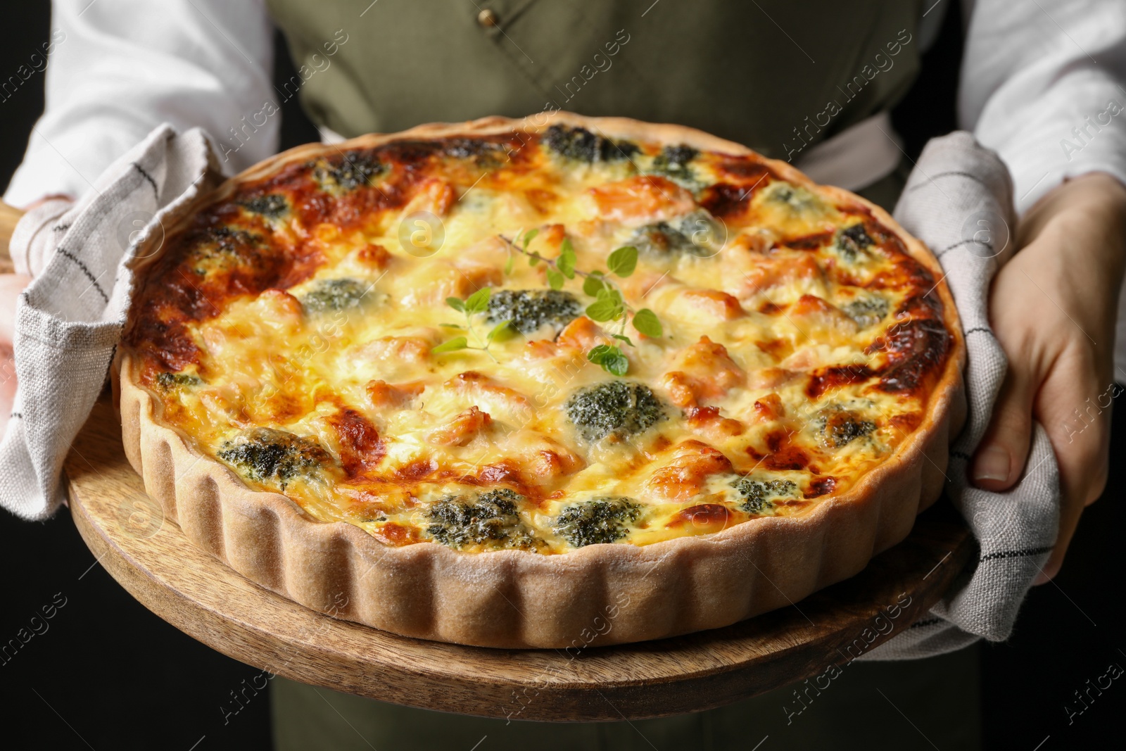 Photo of Woman holding wooden board with delicious homemade salmon quiche on black background, closeup