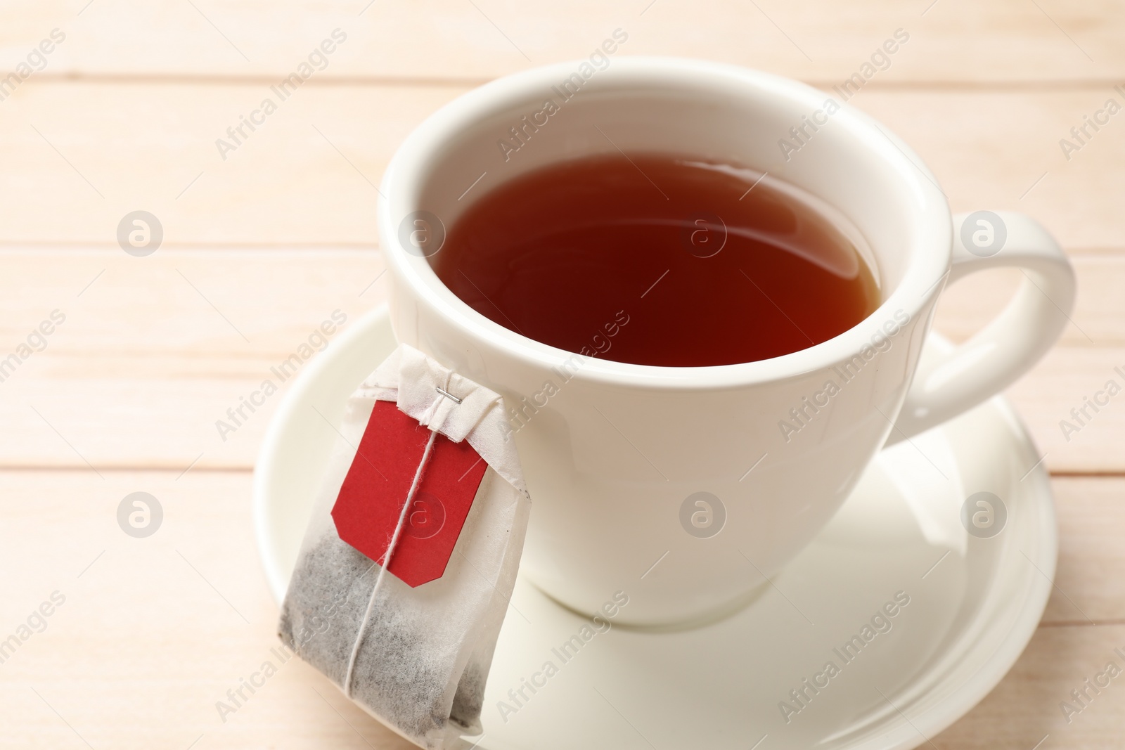 Photo of Tea bag and cup of hot beverage on light wooden table, closeup