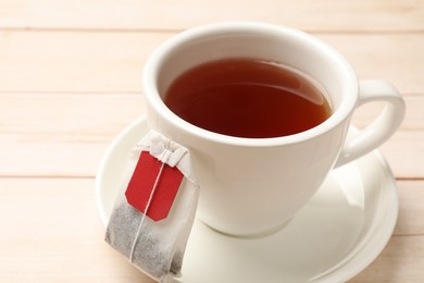 Tea bag and cup of hot beverage on light wooden table, closeup
