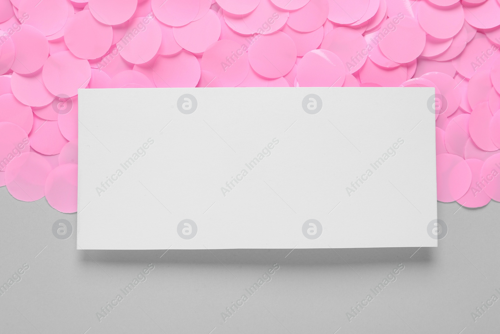 Photo of Blank white card and pink confetti on light grey background,flat lay. Space for text