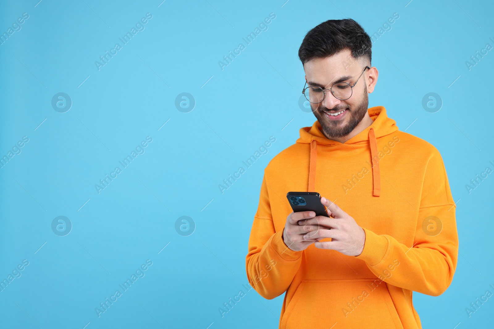 Photo of Happy young man using smartphone on light blue background, space for text