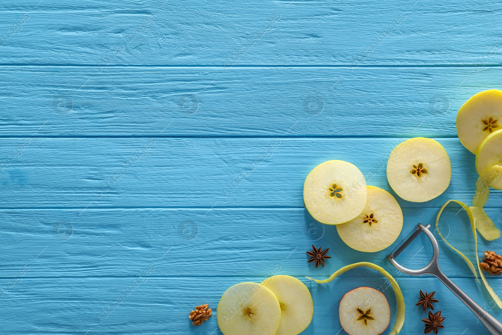 Photo of Food photography. Slices of apple, anise stars, walnuts and peeler on light blue wooden table, flat lay with space for text