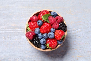 Different fresh ripe berries in bowl on light grey wooden table, top view