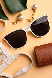 Stylish sunglasses, earrings and brown leather case on beige background, flat lay