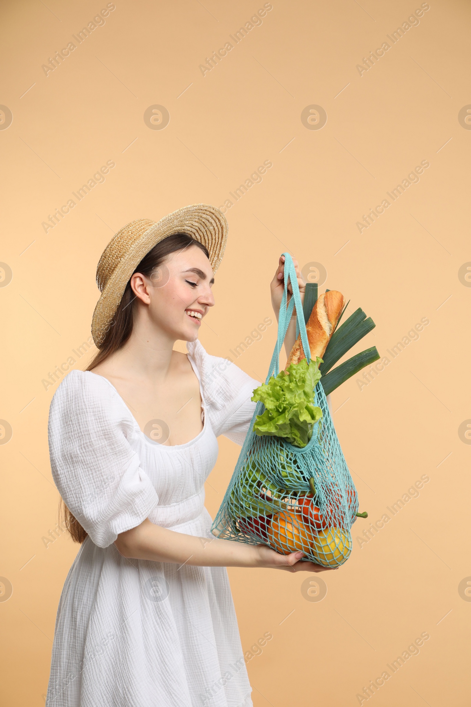 Photo of Woman with string bag of fresh vegetables and baguette on beige background, space for text