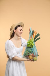 Woman with string bag of fresh vegetables and baguette on beige background, space for text