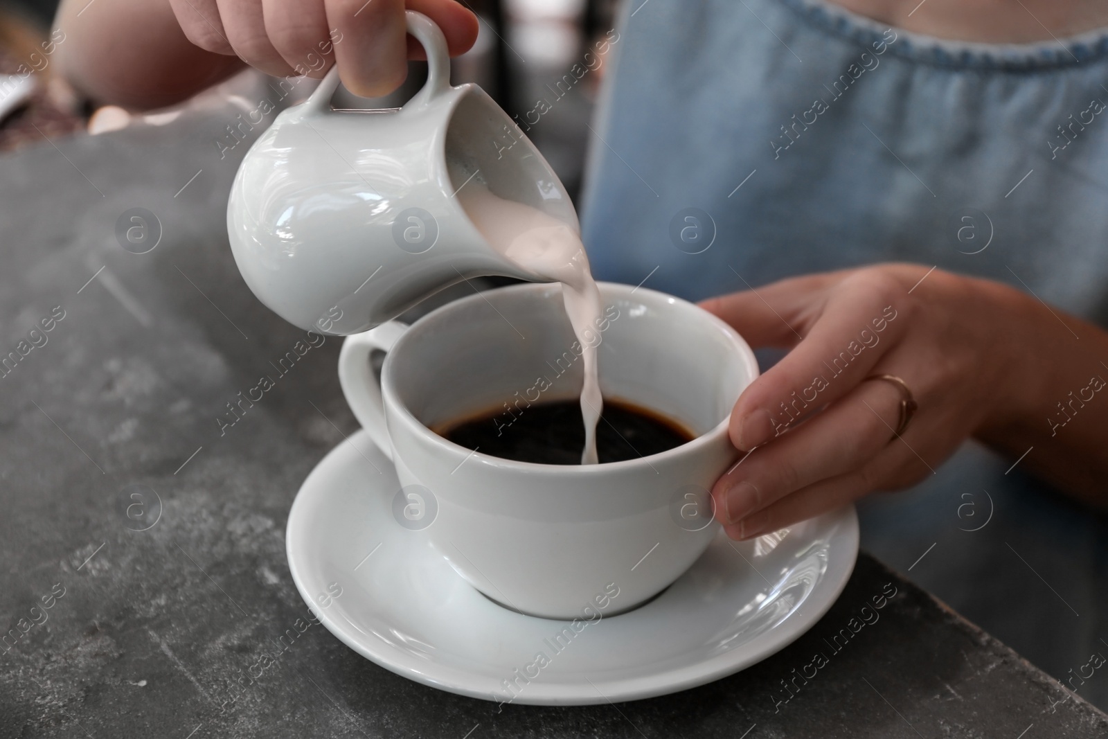 Photo of Woman adding milk to fresh aromatic coffee at table, closeup